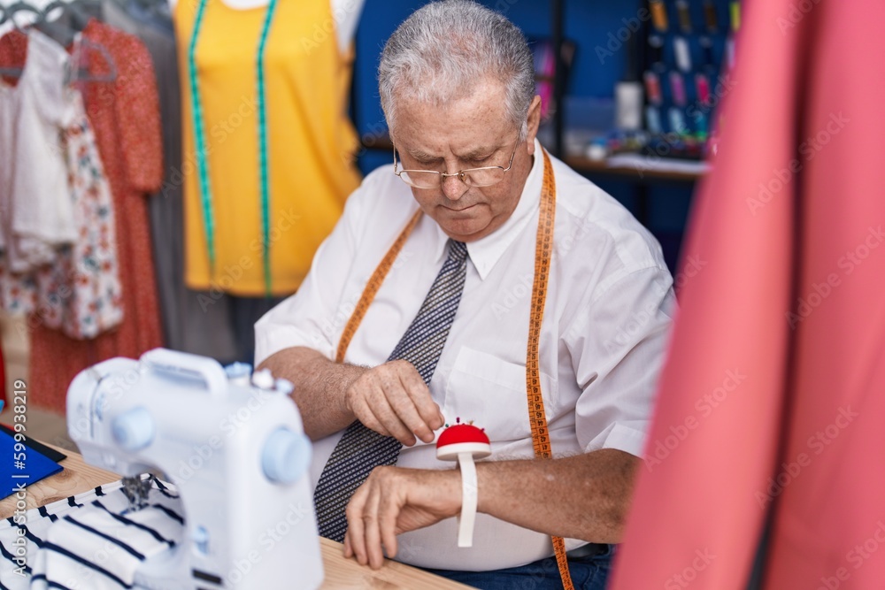 Middle age grey-haired man tailor holding pin at tailor shop