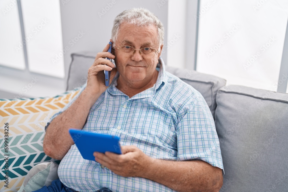 Middle age grey-haired man talking on smartphone using touchpad at home Middle age grey-haired man talking on smartphone using touchpad at home
