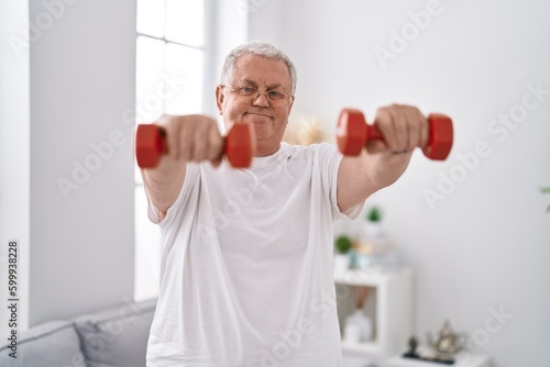 Middle age grey-haired man smiling confident using dumbbells training at home