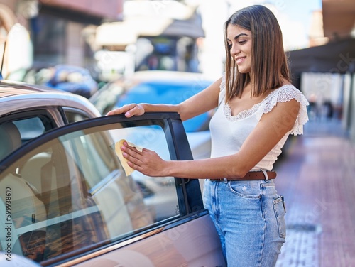Young beautiful hispanic woman smiling confident cleaning glass window car at street