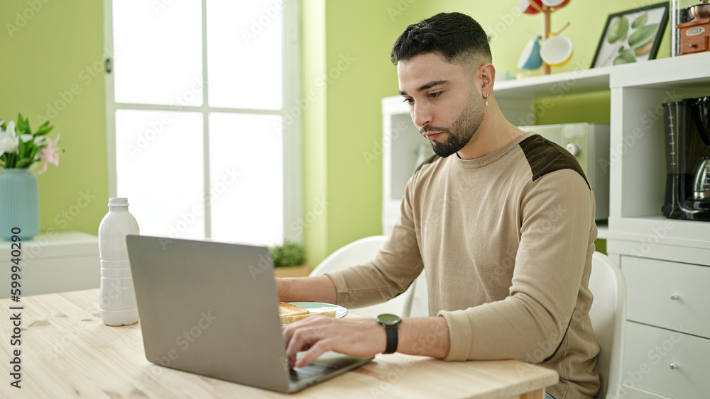 Young arab man using laptop having breakfast at home Young arab man using laptop having breakfast at home