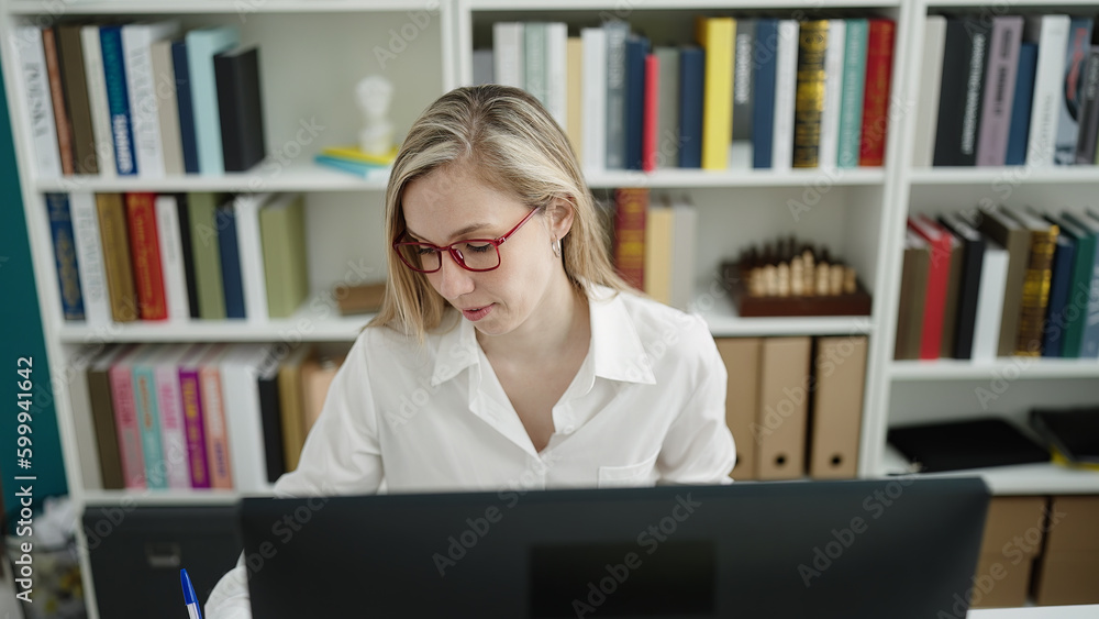 Young blonde woman student using computer writing on notebook at library university Young blonde woman student using computer writing on notebook at library university