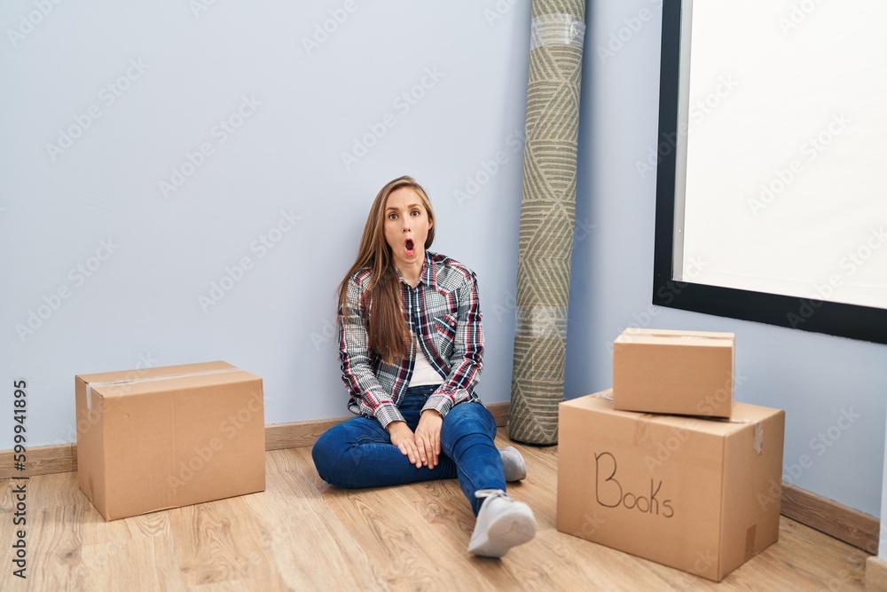 Young blonde woman sitting on the floor moving to a new home afraid and shocked with surprise expression, fear and excited face. Young blonde woman sitting on the floor moving to a new home afraid and shocked with surprise expression, fear and excited face.