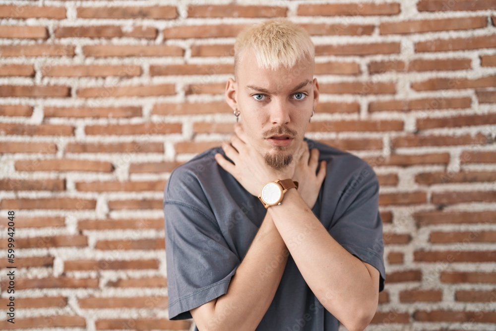 Young caucasian man standing over bricks wall shouting suffocate because painful strangle. health problem. asphyxiate and suicide concept. Young caucasian man standing over bricks wall shouting suffocate because painful strangle. health problem. asphyxiate and suicide concept.