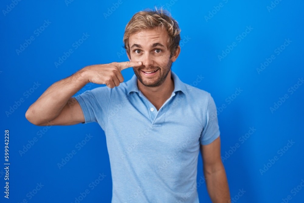 Caucasian man standing over blue background pointing with hand finger to face and nose, smiling cheerful. beauty concept Caucasian man standing over blue background pointing with hand finger to face and nose, smiling cheerful. beauty concept