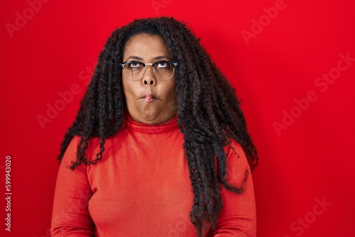 Plus size hispanic woman standing over red background making fish face with lips, crazy and comical gesture. funny expression. © Krakenimages.com