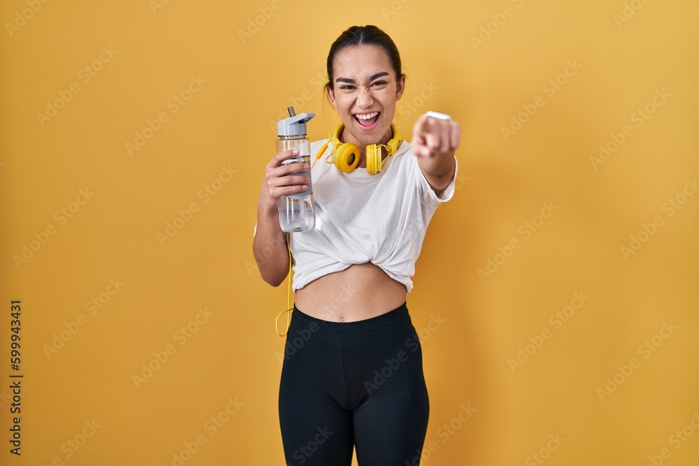 Young south asian woman wearing sportswear drinking water pointing to you and the camera with fingers, smiling positive and cheerful