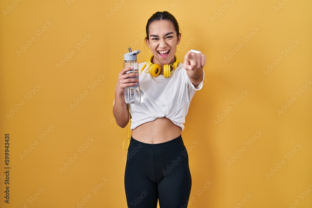 Young south asian woman wearing sportswear drinking water pointing to you and the camera with fingers, smiling positive and cheerful Young south asian woman wearing sportswear drinking water pointing to you and the camera with fingers, smiling positive and cheerful
