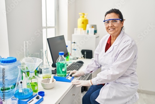 Fototapeta Naklejka Na Ścianę i Meble -  Middle age hispanic woman wearing scientist measuring liquid at laboratory