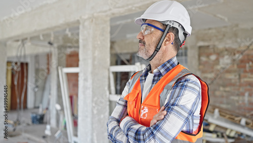 Middle age man builder standing with arms crossed gesture and relaxed expression at construction site