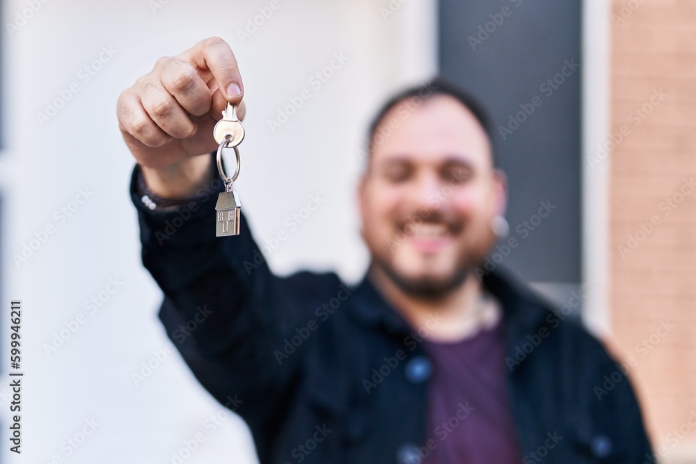 Fototapeta premium Young hispanic man smiling confident holding key of new home at street