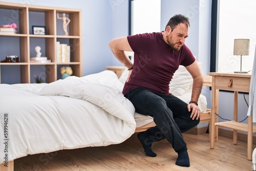 Young hispanic man suffering for backache sitting on bed at bedroom