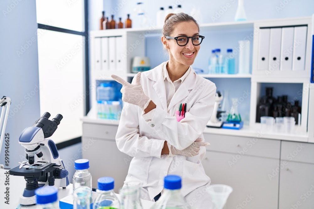 Young woman working at scientist laboratory smiling cheerful pointing with hand and finger up to the side Young woman working at scientist laboratory smiling cheerful pointing with hand and finger up to the side