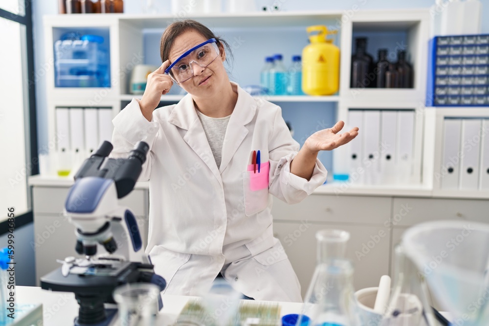 Hispanic girl with down syndrome working at scientist laboratory confused and annoyed with open palm showing copy space and pointing finger to forehead. think about it. Hispanic girl with down syndrome working at scientist laboratory confused and annoyed with open palm showing copy space and pointing finger to forehead. think about it.