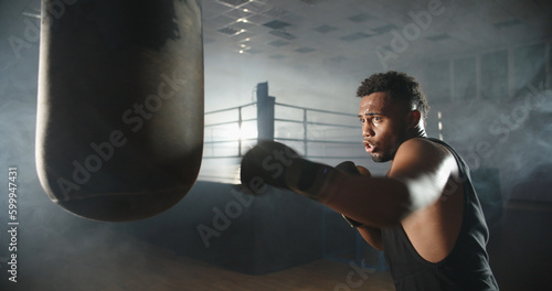 Close up. Handsome african athlete training in a gym, doing a shadow kickboxing art, getting ready for a fight - martial arts, sports concept  © andreybiling
