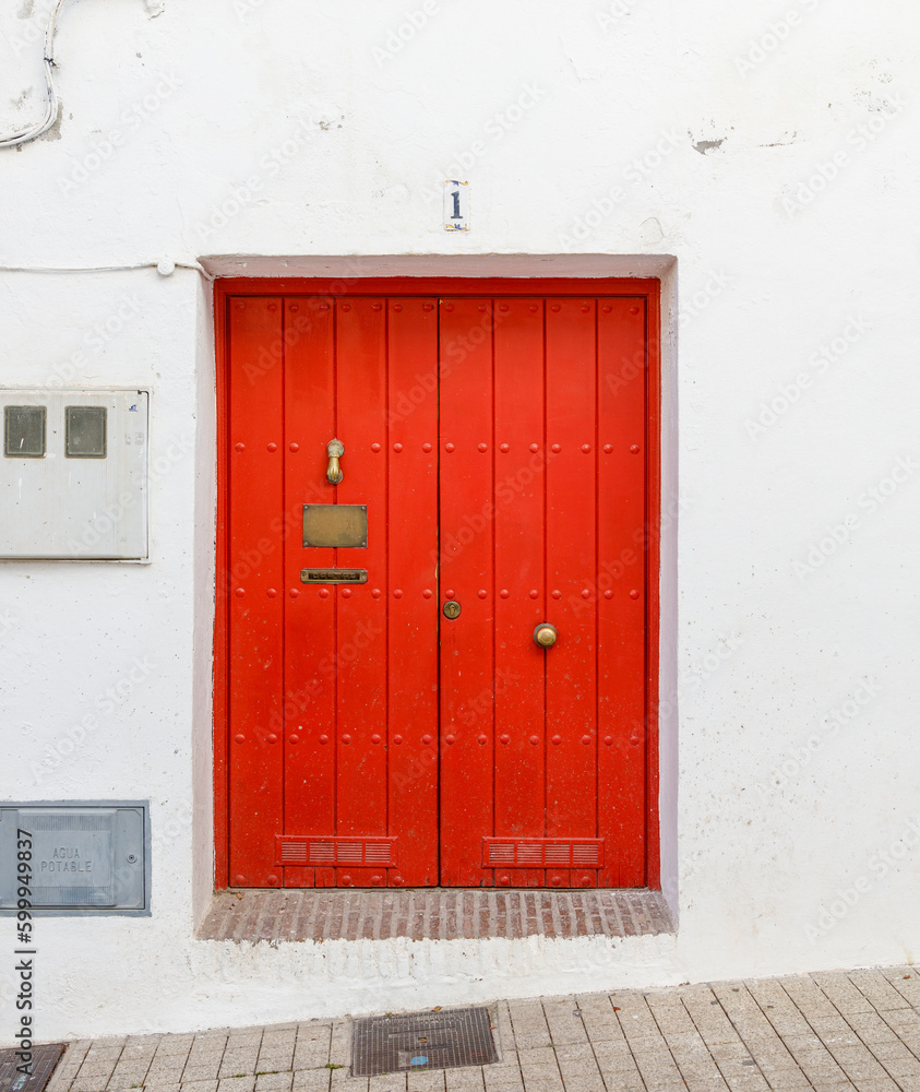 Red wooden door. White building wall, golden doorknocker, tiled sidewalk, wires on the wall, house number. High quality photo