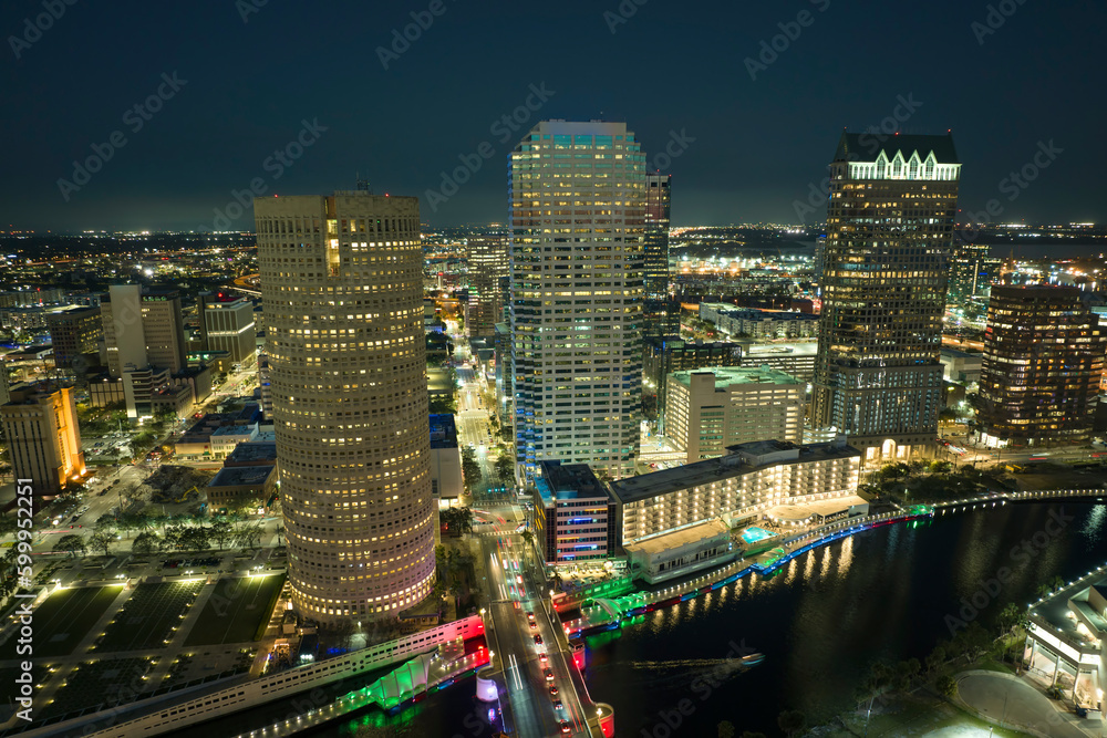 Fototapeta premium View from above of illuminated skyscraper buildings, pedestrian riverwalk and street traffic in downtown of Tampa city in Florida, USA. American megapolis with business financial district at night
