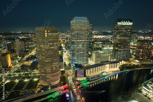 View from above of illuminated skyscraper buildings, pedestrian riverwalk and street traffic in downtown of Tampa city in Florida, USA. American megapolis with business financial district at night