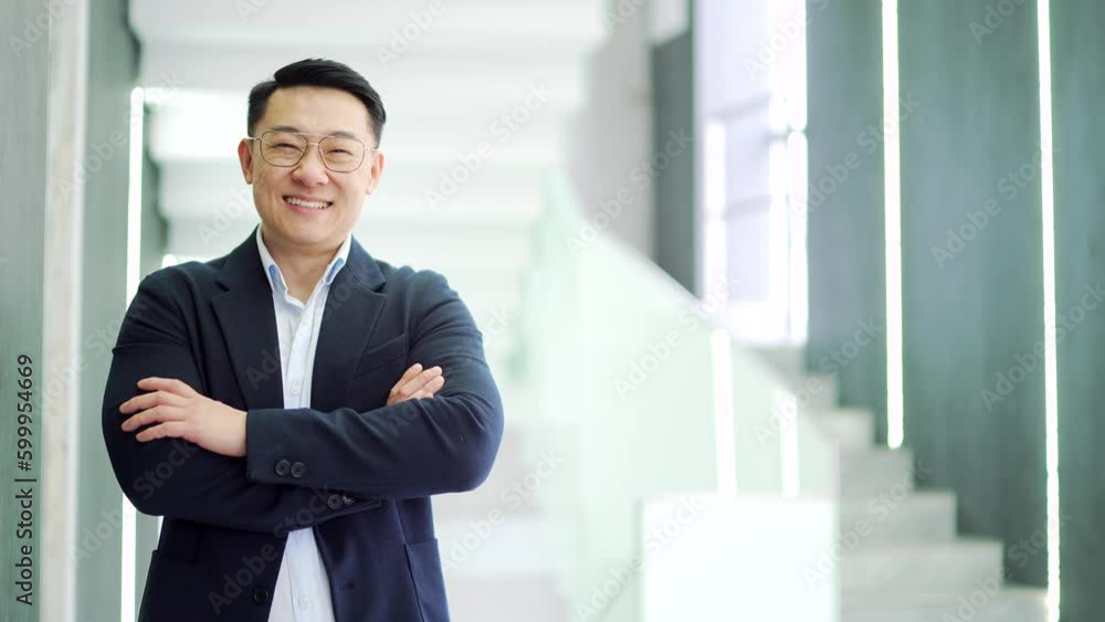 Portrait of a smiling Asian businessman in a formal suit standing in a modern office building. Happy owner, boss, investor with crossed arms and looking at camera. Empty copy space for writing text Portrait of a smiling Asian businessman in a formal suit standing in a modern office building. Happy owner, boss, investor with crossed arms and looking at camera. Empty copy space for writing text