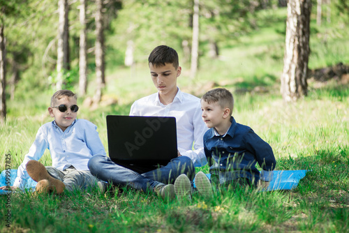 children sit in the park and play on the laptop