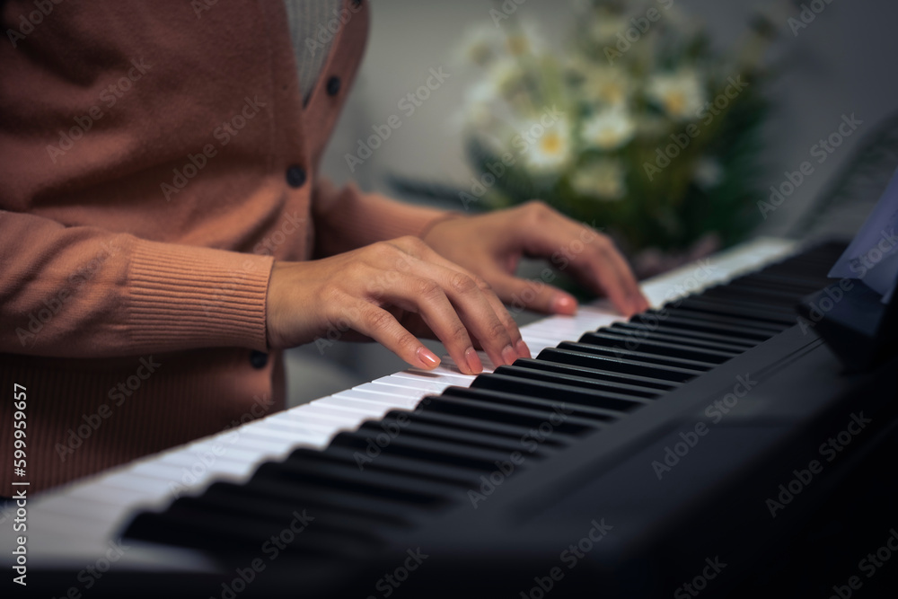 Fototapeta premium Croped Asian woman hand put on piano key to preparing to play music, closed up girl hand on music instrument with blur flower background.