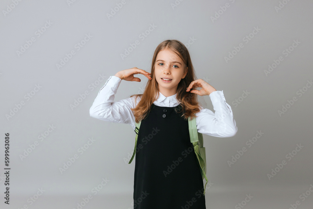 cheerful teenage girl 11,12,13 years old in a school uniform wears a backpack on a gray background. school fashion cheerful teenage girl 11,12,13 years old in a school uniform wears a backpack on a gray background. school fashion
