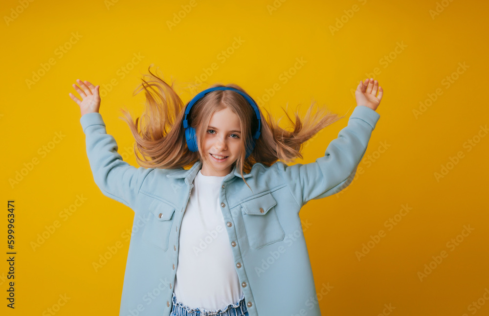 A young girl 11-13 years old in headphones listens to music and dances in the studio on a yellow background A young girl 11-13 years old in headphones listens to music and dances in the studio on a yellow background