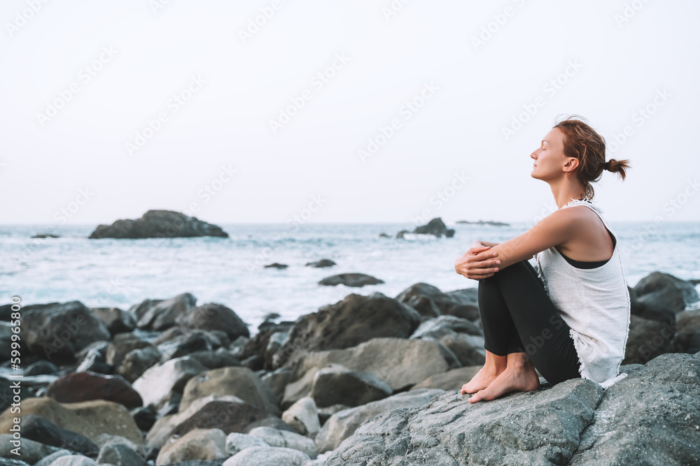 Woman is practicing yoga, meditating on the beach.