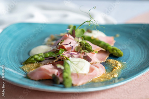 Fotografie Selective focus of an appetizer with asparagus, taleggio, peanuts and rosemary ham on a blue plate