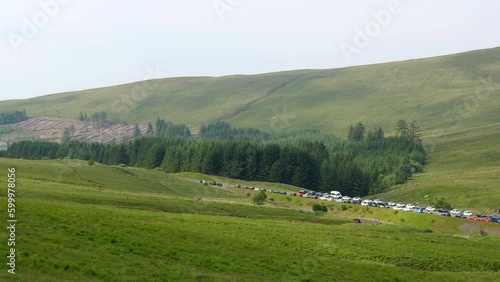 Handheld panning shot from hill of many vehicles parked on roadside of A470 road and in Pont ar Daf car park at the start of popular route to Pen y Fan peak in Brecon Beacons National Park in Wales. photo