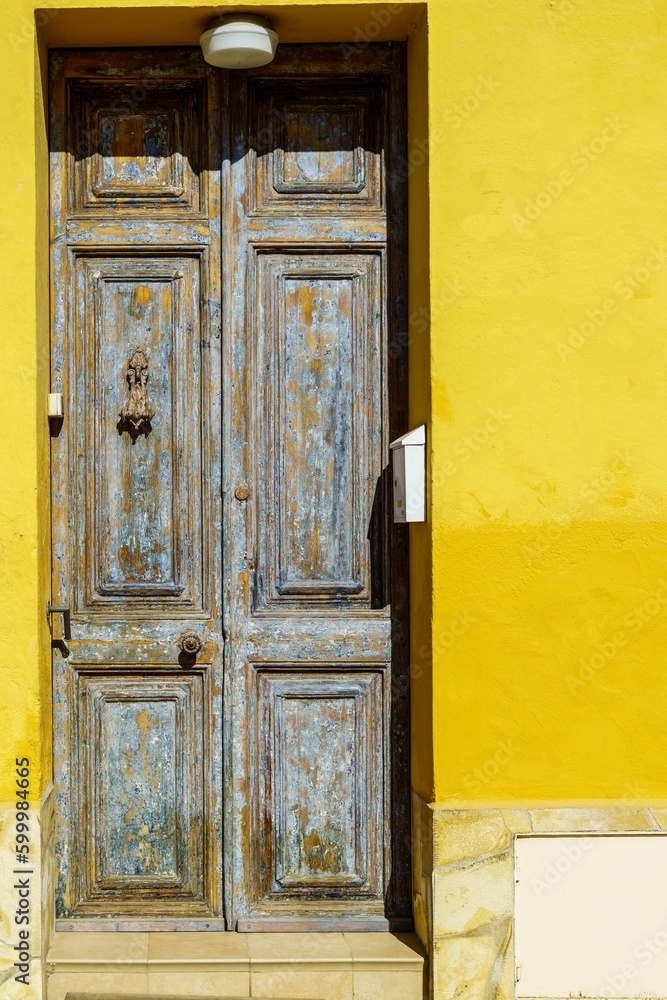 A beautiful old Mediterranean house in a residential district, with its yellow-painted wood door and wall providing security from the sun.
