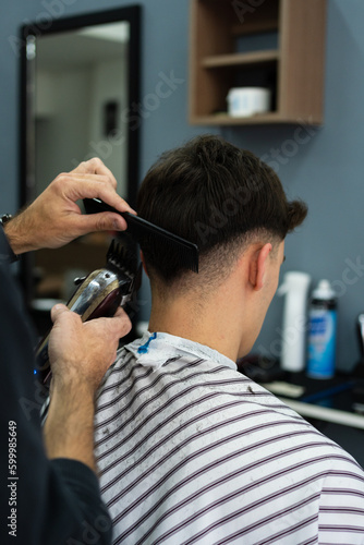 Barber's hands cutting the hair of a young man. Rear and vertical view