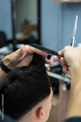 Hairdresser holding a male client's hair with his hands and a comb. Veritcal photo