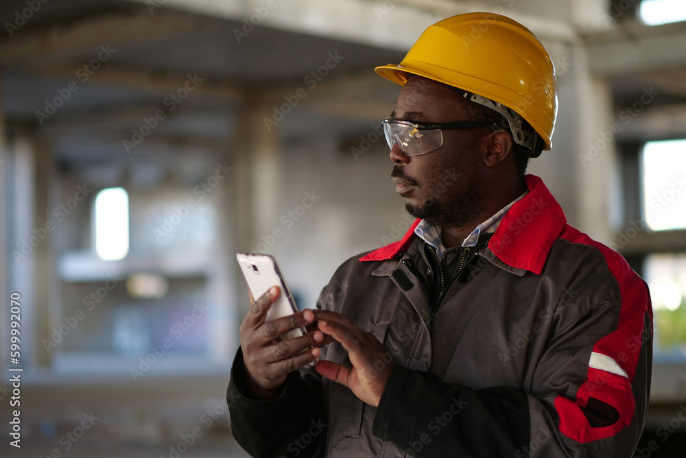 African american workman with smartphone at construction site African american workman with smartphone at construction site