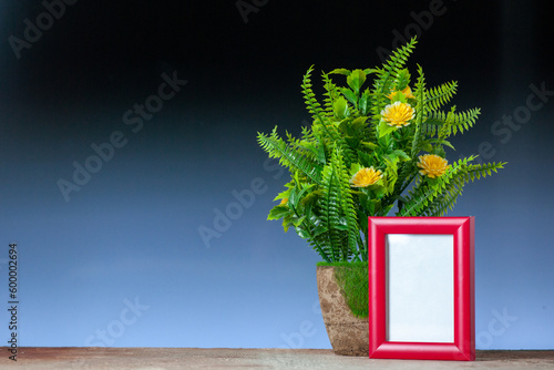 Top view of red empty picture frame standing on table and beautiful flower pot on black blue mix colors background with free space