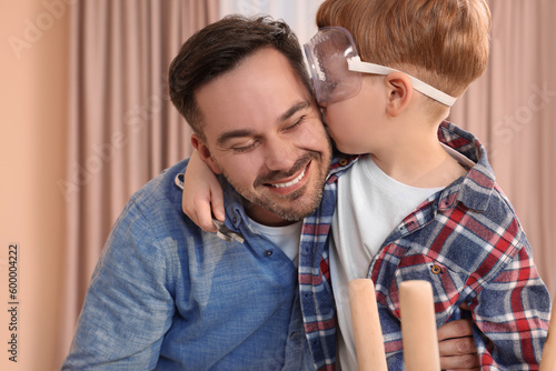 Son in protective glasses kissing father indoors. Repair work photo