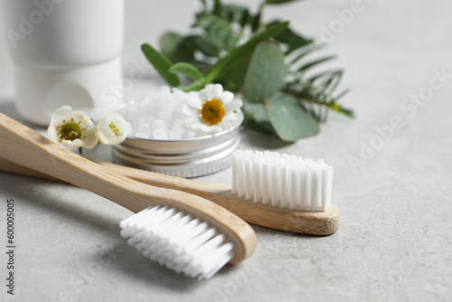 Bamboo toothbrushes, flowers and sea salt on light grey table, closeup