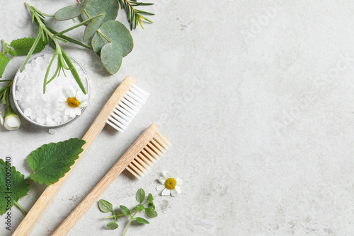 Bamboo toothbrushes, flowers and herbs on light grey table, flat lay. Space for text