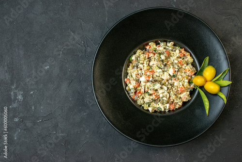 Top view of delicious salad served with kumquats with stem on a black plate on the left side on dark background