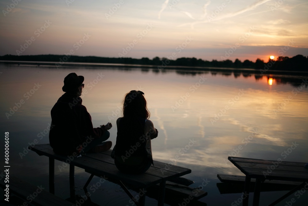 friends sitting on a bench meditating and viewing the sunset in a lake friends sitting on a bench meditating and viewing the sunset in a lake