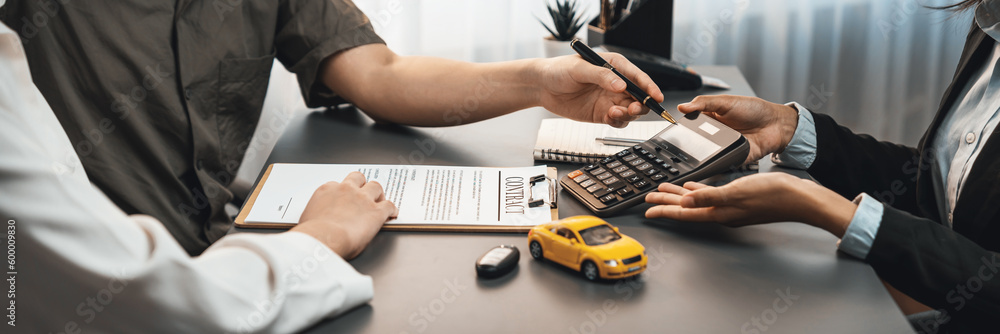 Φωτογραφία Car dealer calculate interest rate and costs of car loan with calculator, explaining details to customer on term and agreement in dealership office, offering financial and insurance service