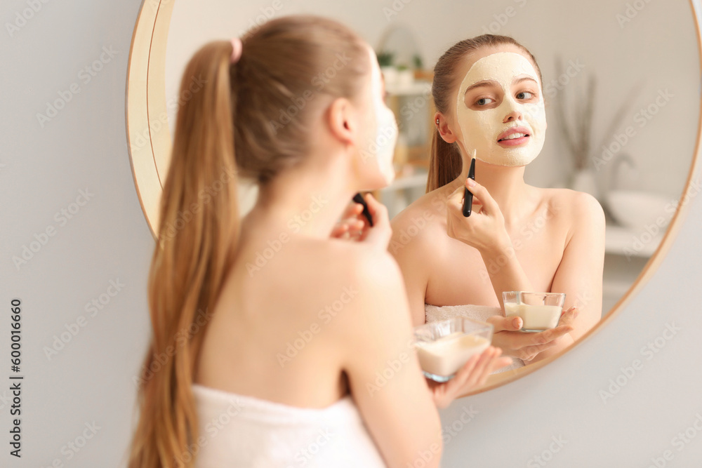 Young woman applying turmeric mask with brush near mirror at home Young woman applying turmeric mask with brush near mirror at home