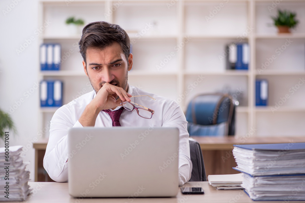 Naklejka premium Young male employee and too much work at workplace