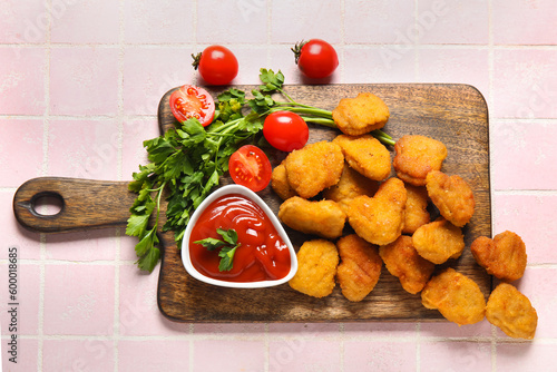 Board with delicious nuggets, bowl of ketchup and parsley on pink tiled table