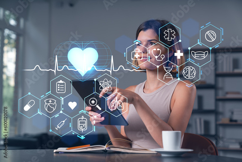 Smiling businesswoman in casual wear holding tablet device touching it at office workplace. Concept of distant work, business education, information technology. Health care icons hologram