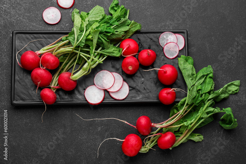 Board of fresh radishes with leaves on dark background