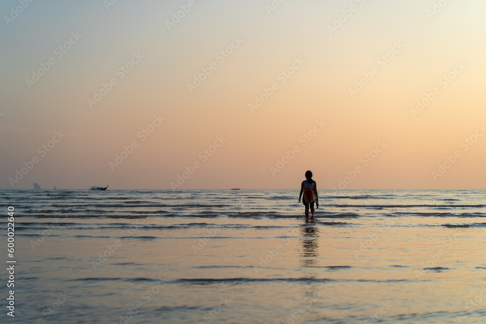 back asian child or kid girl walking on sea beach in summer island and people happy relax with golden sunlight in evening sunset or morning sunrise to tourist fishing boat for vacation travel holiday