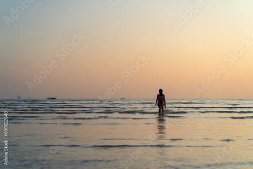 back asian child or kid girl walking on sea beach in summer island and people happy relax with golden sunlight in evening sunset or morning sunrise to tourist fishing boat for vacation travel holiday © kornnphoto