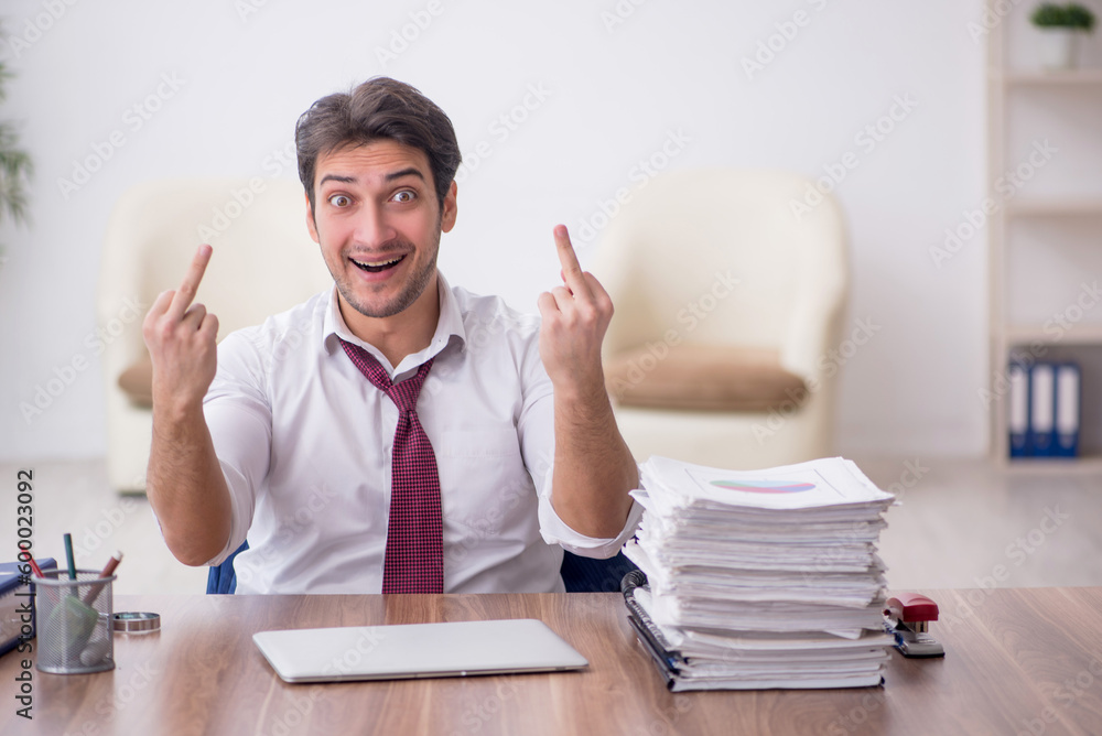 Young male employee unhappy with excessive work in the office Young male employee unhappy with excessive work in the office