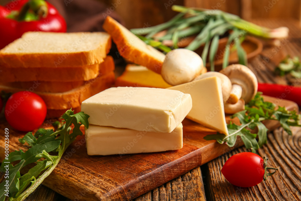 Board with processed cheese, bread and vegetables on brown wooden background Board with processed cheese, bread and vegetables on brown wooden background